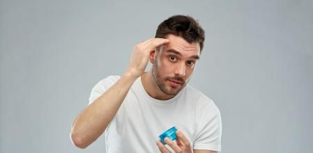 beauty, hairstyle, haircare and people concept - happy young man styling his hair with wax or gel over gray background