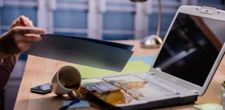 Spilled coffee on laptop, woman holding file.