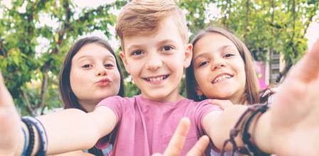 Best friends taking selfie outdoors in backyard – happy friendship with smart kids having fun celebrating summer vacation – modern children enjoying time together at garden party playing and smiling