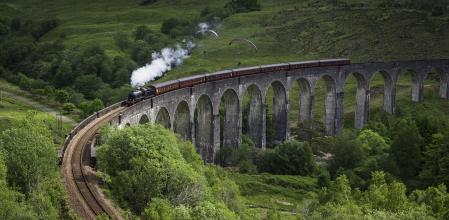 White smoke puffing evocatively from a historic steam train thundering across the iconic arches of the Glenfinnan Viaduct over a green mountain glen deep in the Highlands of Scotland, UK. ProPhoto RGB profile for maximum color fidelity and gamut.