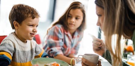 Displeased boy refusing to eat during breakfast with his single mother and sister in dining room.