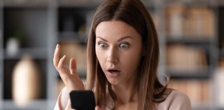 Head shot close up young shocked woman looking at mobile phone screen, received bank debt notification. Stunned frustrated lady reading sms with unbelievable news on smartphone, making big eyes.
