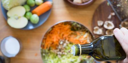 Pouring olive oil from bottle onto cabbage and carrot salad. Selective focus