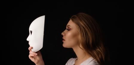 Profile view of blond woman holding white mask acting out and pretending, feeling depressed