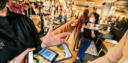 foto ilustracion XAVIER CERVERA 25/11/2021 un cliente con su pasaporte covid en google drive d su terminal mobil y una camarera con dispositivo electronico (tablet o ipad o mobil tb) verifica con la web de catsalut q es valido el pasaporte covid del cliente q quiere entrar en el interior del restaurante o bar (para terraza no hace falta)