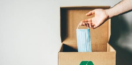 Un hombre tira una mascarilla a una caja reciclab