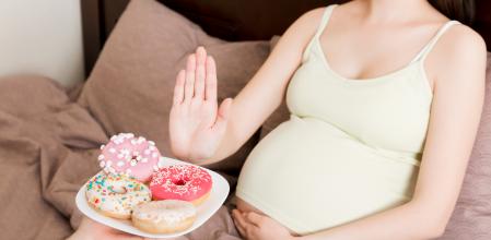 Close up of pregnant woman staying in bed rejects to eat junk food such as donuts and makes no gesture. Healthy diet for future mother concept.