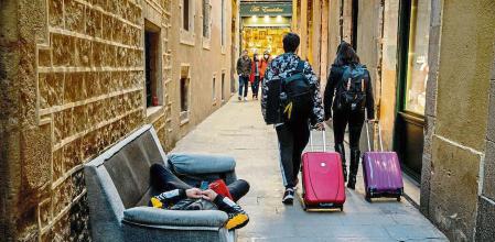 FOTO ALEX GARCIA RECUPERACION TURISMO COVID. DOS JOVENES CON MALETAS PASAN JUNTO A UN INDIGENTE EN UNA CALLE DEL GOTICO DE BARCELONA 2022/02/22