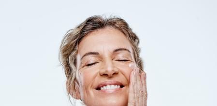 Una mujer sonriente se aplica una crema en el rostro