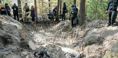Journalists stand on the side of a mass grave of village residents and the village head and his family, in the village of Motyzhyn, close to Kyiv, Ukraine, Monday April 4, 2022. Russia is facing a fresh wave of condemnation after evidence emerged of what appeared to be deliberate killings of civilians in Ukraine. (AP Photo/Efrem Lukatsky)
