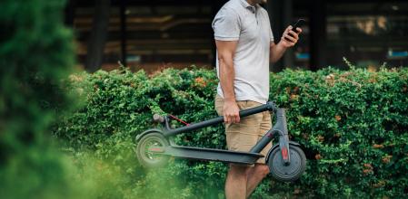 Un hombre lleva plegado su patinete eléctrico en la mano