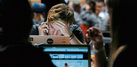 An attendee uses a mobile phone whilst looking at his laptop computer screen in the TechCrunch Disrupt London 2015 Hackathon in London, U.K., on Saturday, Dec. 5, 2015. Disrupt is an annual conference hosted by TechCrunch where some technology startups launch their products and services competing on stage in front of venture capital potential investors, media and other interested parties. Photographer: Luke MacGregor/Bloomberg