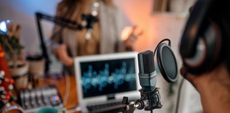 Selective focus of microphone used by young man and woman while recording podcast during interview and doing live broadcast in studio