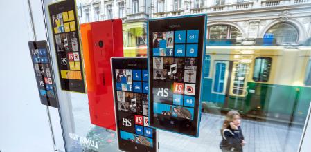 A pedestrian talks on her mobile phone as she looks at promotional material for Nokia Oyj's windows based Lumia mobile phones in the window of the company's store in Helsinki, Finland, on Tuesday, Sept. 3, 2013. Microsoft Corp. agreed to buy Nokia OyjÕs handset unit and license its patents for 5.44 billion euros ($7.2 billion), seeking to revive two smartphone businesses that have struggled for a half-decade to gain share against Apple Inc. and Google Inc. Photographer: Tomi Setala/Bloomberg