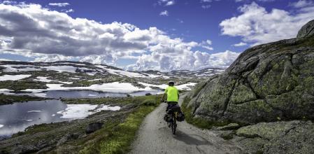 Norway, summer 2014. Young man bicycles Rallarvegen, that runs between Haugastøl and Flåm. Hardangervidda National Park. Beautiful scenery with small lakes and high mountains. Sunny and warm, but still a little snow.