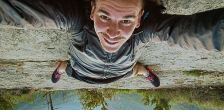 30 years man smiling taking a selfie up side down on the ground with the beautiful nature views of the Garrotxa region on sunrise moment with the morning light and the mountains.