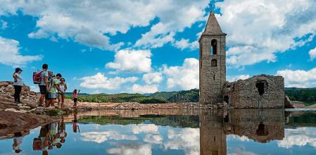 People stand in front of the ruins of the church of Sant Roma de Sau, at the swamp of Sau, located in the province of Girona in Catalonia on August 23, 2022. - The swamp of Sau is a reservoir on the Ter river, created by a dam located in the municipality of Vilanova de Sau. The marsh, built from 1947 to 1962, covered the village of Sant Roma de Sau which is still visible, including the bell tower of the 11th century Romanesque church, when the reservoir water level is low. The church of the Sau swamp is registered as the world's oldest that is preserved upright in water. (Photo by Josep LAGO / AFP)