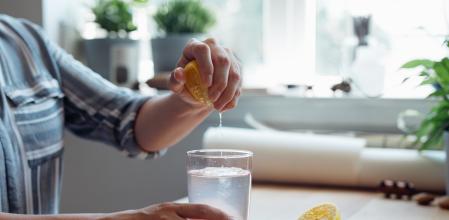 Close up shot of an anonymous young woman's hands squeezing a lemon into a cup of water making lemonade sitting at a wooden table.