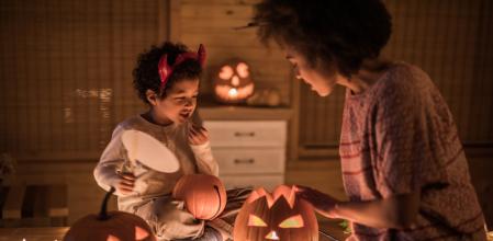 African American single mother decorating pumpkins with her small son on Halloween. Focus is on boy.