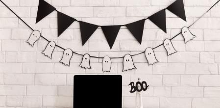 Halloween decorations in modern office with laptop, black blank screen, copy space for advertisement