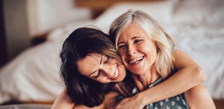 Beautiful adult granddaughter hugging beautiful senior grandmother while sitting on the sofa dinking coffee