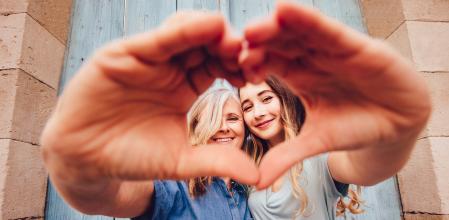 Cheerful grandmother and teenage granddaughter forming a heart shape with their hands in old town
