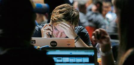 An attendee uses a mobile phone whilst looking at his laptop computer screen in the TechCrunch Disrupt London 2015 Hackathon in London, U.K., on Saturday, Dec. 5, 2015. Disrupt is an annual conference hosted by TechCrunch where some technology startups launch their products and services competing on stage in front of venture capital potential investors, media and other interested parties. Photographer: Luke MacGregor/Bloomberg
