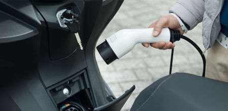 Un usuario de una moto eléctrica recarga su vehículo en una conexión