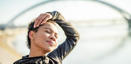 Happy athletic African American woman doing neck stretching exercises outdoors.