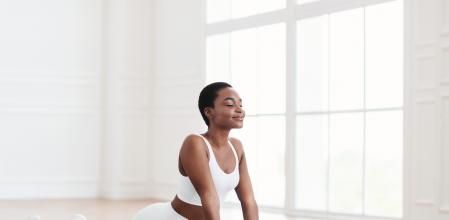 Calm millennial black woman practicing yoga, doing Ardha bhudjangasana, Sphinx exercise, baby Cobra pose, working out, wearing sportswear, white leggings and bra top, indoor full length, yoga studio