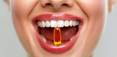 Vitamins And Food Supplements. Close Up Of Beautiful Woman Opened Mouth Holding Fish Oil Pill In White Teeth. Smiling Girl Holding Capsule With Omega-3 Between Teeth. Healthy Diet Nutrition Concept
