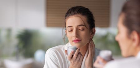 Beautiful young woman smelling fragrance of face cream
