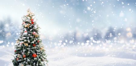 Beautiful Festive Christmas snowy background with holiday lights. Christmas tree decorated with red balls and knitted toys in forest in snowdrifts in snowfall on nature outdoors, panoramа, copy space.