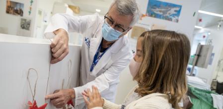 Complicidad.El médico Constantino Sábado, del servicio de oncología y hematología pediátrica del hospital, ayuda a Ànnia a colgar las estrellas rojas que adornan el centro