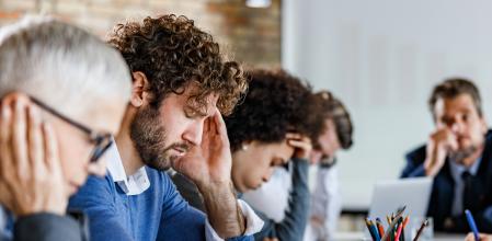 Group of entrepreneurs feeling frustrated during a meeting in the office. Focus is on man with headache.