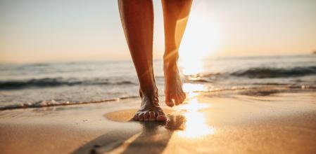 Close-up of female legs getting out of the sea water and walking on sandy beach at beautiful sunset