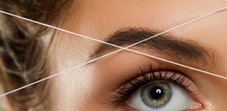 Close-up of female eye with a thread. Eyebrow threading - epilation procedure for brow shape correction