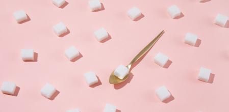 Geometrical pattern with white sugar cubes and a teaspoon on pastel pink background