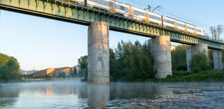 El tren pasa por el puente mientras el río Ter humea.