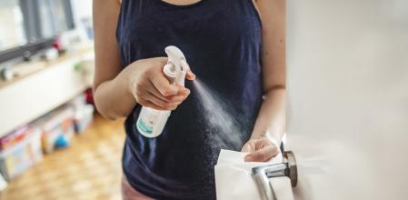 Woman cleaning a door handle with a disinfection spray and disposable wipe. Woman sanitizing door handle with antibacterial spray. Girl staying at home during coronavirus outbreak