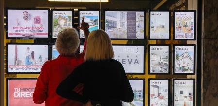 Una pareja mirando el escaparate de una inmobiliaria con las ofertas de pisos y casas de alquiler y venta.