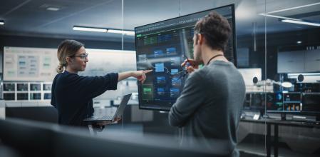 Two Diverse Software Developers Having a Meeting in a Conference Room. Female and Male Tech Industry Engineers Brainstorming Ideas for Their Neural Network Blockchain Startup