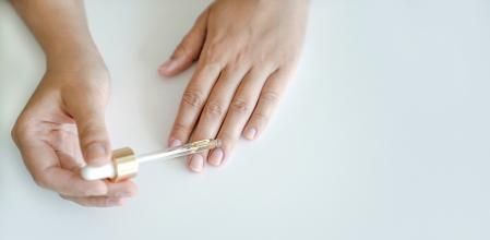 Una personas aplicándose aceite de vitaminas para las uñas.