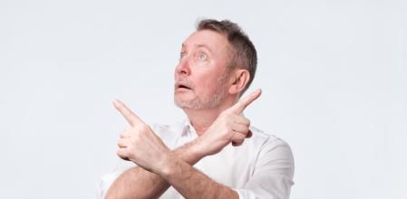Senior man feeling uncertain having two choices. Unsure mature guy crossing hands on chest and pointing left and right in both directions hesitating which way choose