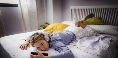 Bored teenager girl laying on her bed using phone and listening music. High resolution 42Mp studio digital capture taken with SONY A7rII and Zeiss Batis 25mm F2.0 CF lens