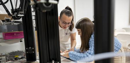 Andrea, con polo blanco, enseña a Inés algunas piezas realizadas en impresión 3D, reportaje sobre un programa para invitar a las chicas a desarrollar formación profesional Steam, en la Escola De Treball, Barcelona, 4 de Marzo de 2024.