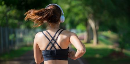 Young fitness sports women runner running in the park. Happy athletic woman listening music on earphones while running in nature in the morning. Healthy fitness woman jogging outdoors.