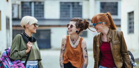 Three female friends, living alternative lifestyle, going together to skate park or music festival. Redhead, blonde and girl with dreadlocks and tattoos sharing moments.