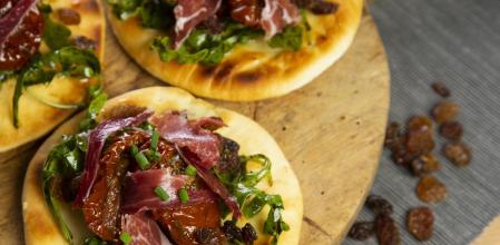 Cómo hacer mini pizzas de tomates secos, rúcula, jamón ibérico y pasas