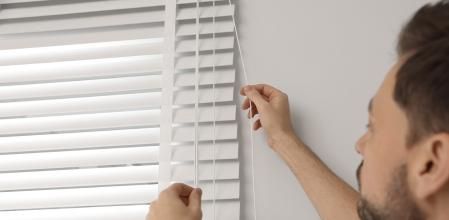 Una personas abriendo una persiana veneciana.